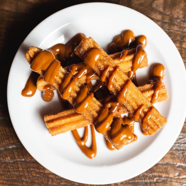 Golden churros drizzled with rich caramel sauce, served on a white plate at Friducha.