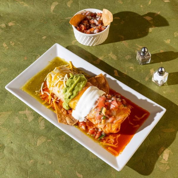 A Friducha burrito covered in green and red sauce, guacamole, sour cream, and pico de gallo.