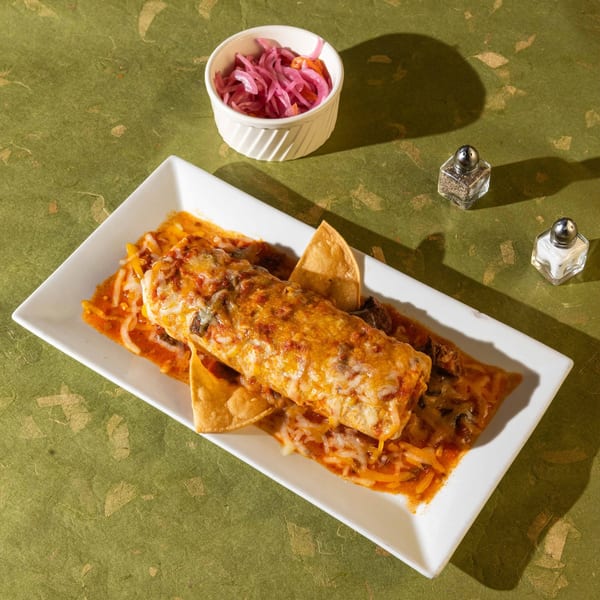 A Friducha Mexican burrito covered in melted cheese and sauce, with tortilla chips and pickled onions.