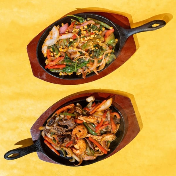 Two sizzling fajita platters on a yellow background, one vegetarian and one with shrimp, chicken, and steak.