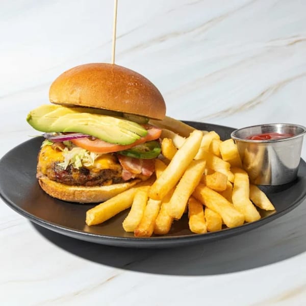 A Friducha burger with avocado, bacon, cheese, and vegetables, served with fries and ketchup.