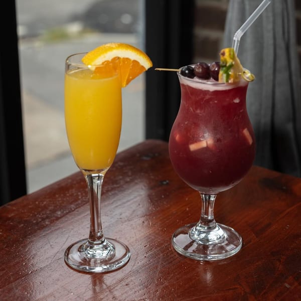 Two cocktails, one orange mimosa and one red sangria with fruit, on a wooden table.
